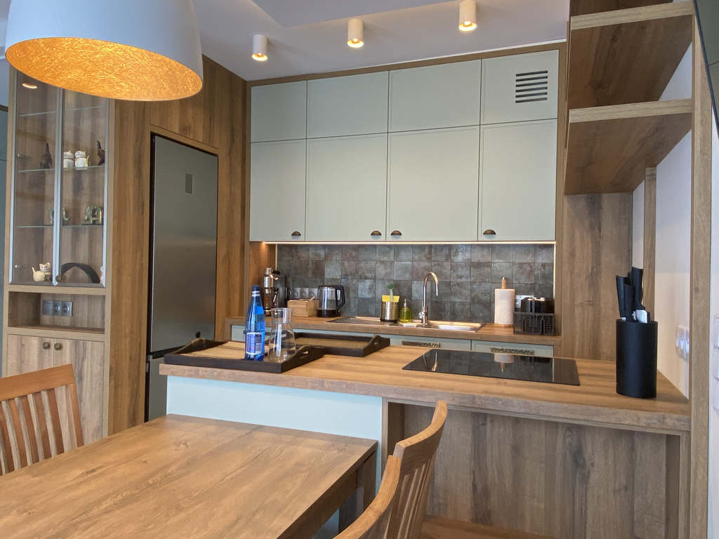 Küchenzeile der Camilla Suite mit Induktionskochfeld, hellen Hängeschränken und Esstisch aus Holz