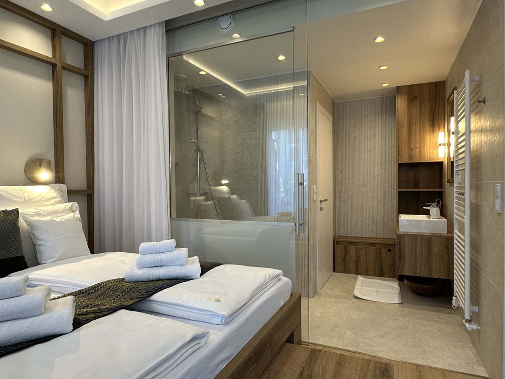 Schlafbereich der Camilla Suite mit Doppelbett und offenem Glas-Badezimmer mit Dusche