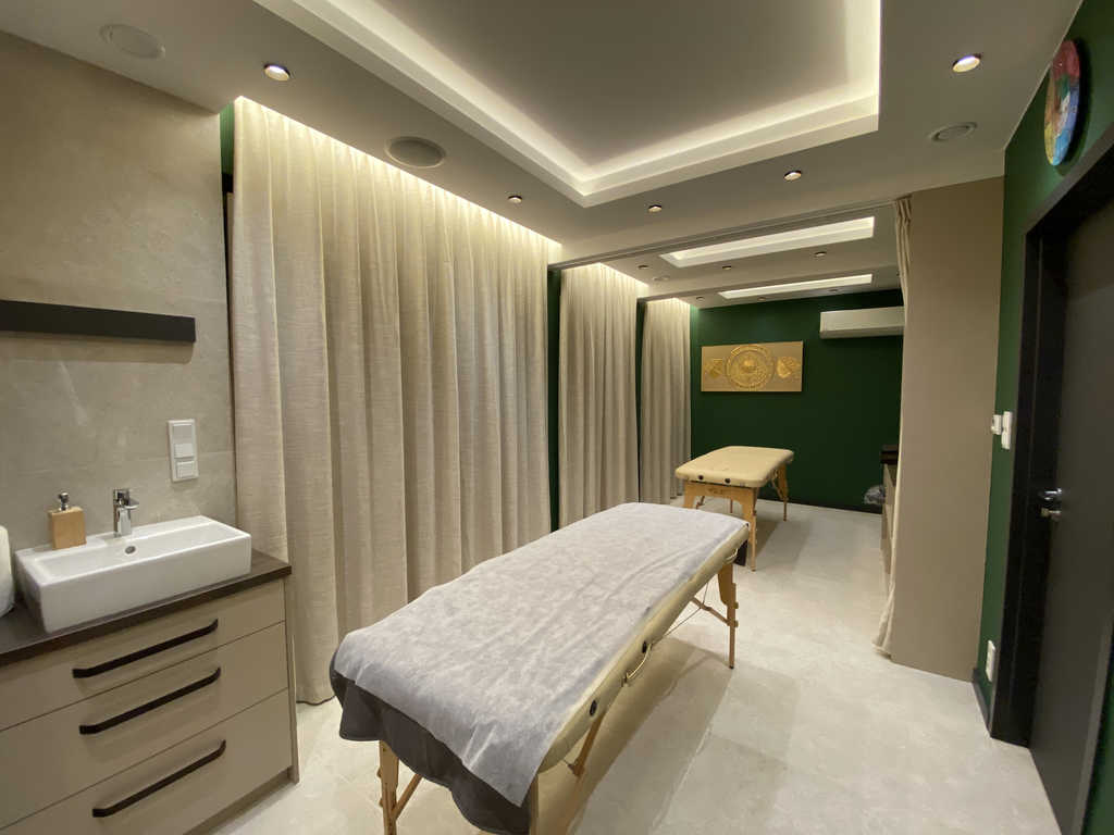 Behandlungsraum im ARALIYA Krakau mit Massageliege, Waschtisch und beigen Vorhängen an grüner Wand