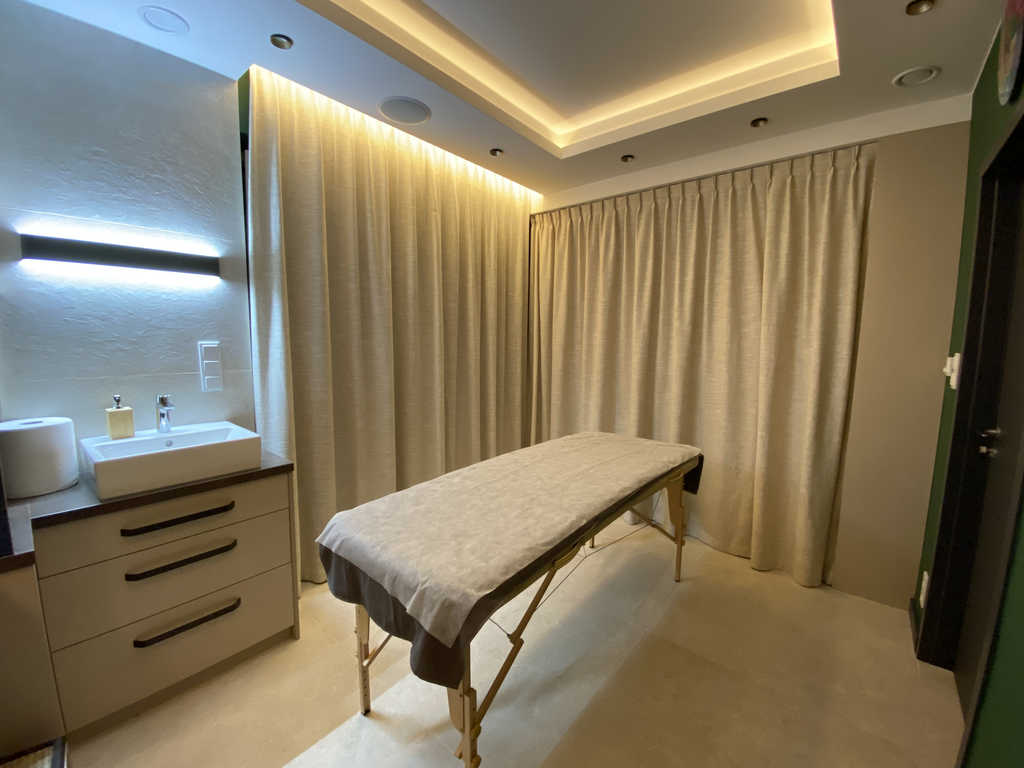 Behandlungsraum im ARALIYA Krakau mit Massageliege, Waschbecken und beleuchtetem Spiegel