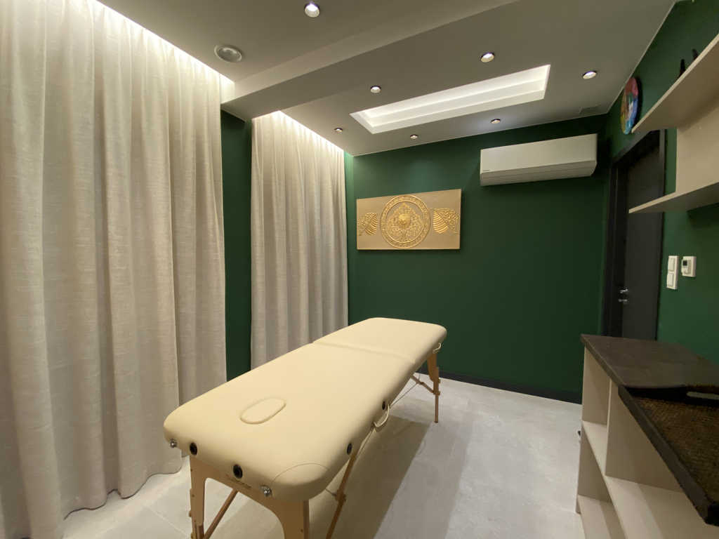 Behandlungsraum im ARALIYA Krakau mit Massageliege vor grüner Wand und goldenem Relief