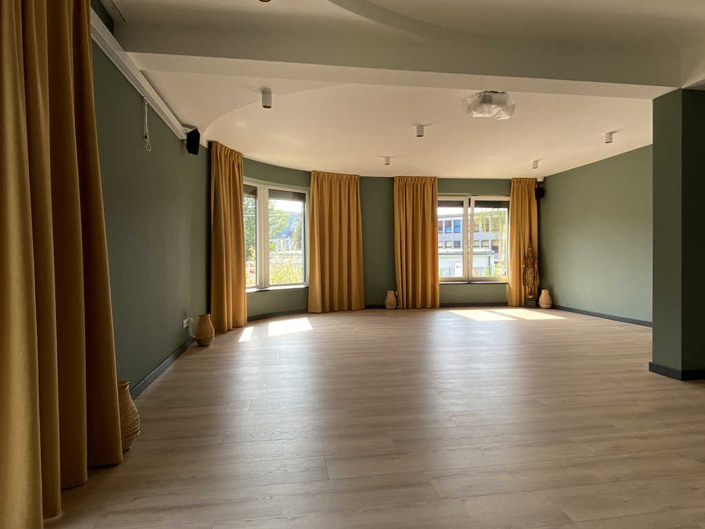 Großer Bewegungsraum im ARALIYA Krakau mit Holzboden, gelben Vorhängen und Fensterfront