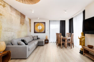 Wohnzimmer der Queen Suite mit Ecksofa, goldgetönter Steinwand und Essplatz am Fenster