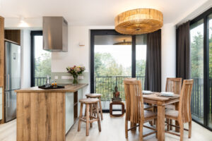 Essbereich der Cosmea Suite mit Holztisch, Kücheninsel, Rattan-Deckenleuchte und bodentiefen Fenstern zum Grün